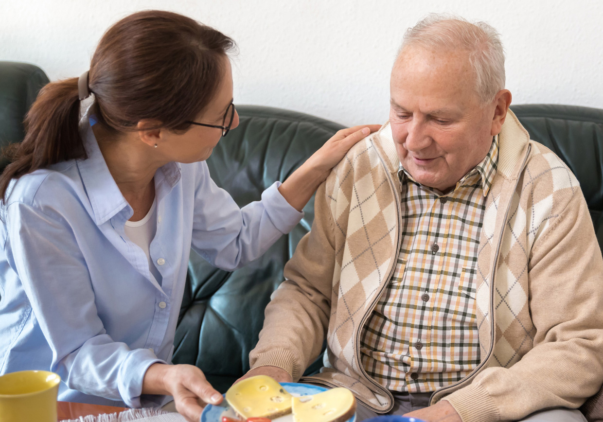 Eine Dame legt die Hand auf die Schulter eines Patienten im Pflegeheim